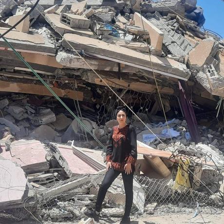 صورة سماح كساب مسؤولة البرنامج الإنساني في مؤسسة أكشن إيد-فلسطين وهي تقف بين الدمار الذي احدثته  الغارات الجوية الإسرائيلية 