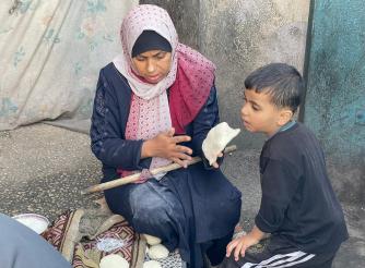 صورة لأمرأة فلسطينية في أحدمراكز الإيواء تحاول إعداد الخبز لإطعام طفلها في ظل انتشار المجاعة بسبب التصعيد العسكري ضد قطاع غزة – قطاع غزة لعام 2024